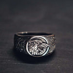 Chevalière viking ornée du sceau du loup fenrir qui tente de sortir de l'anneau qui l'encercle afin de s'attaquer au symbole de l'yggdrasil - bague pour homme posée sur table en bois nordique