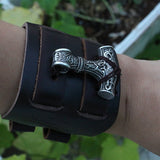 bracelet manchette viking en cuir ornée du symbole nordique du Mjolnir, le marteau de thor - photo sur fondf orêt porté par homme 0- vue de face du bracelet