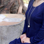 collier et pendentif oeil d'argent portée par femme tenue bleue en méditation dans une forêt