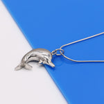 collier à pendentif à la forme d'un dauphin en argent massif . Bijou pour femme photographié sur fond bleu et blanc