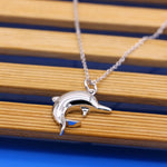 collier à pendentif à la forme d'un dauphin en argent massif . Bijou pour femme photographié sur bois